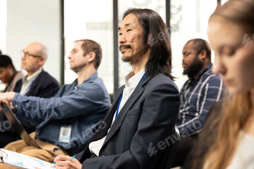 Preview: Asian male participant taking notes on clipboard papers in the audience