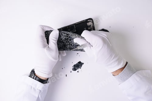 Preview: Technician with rubber gloves repairing broken smartphone with tools at a white table