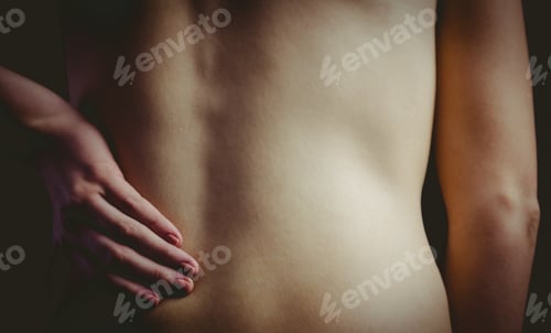 Preview: Nude woman with a back injury on black background