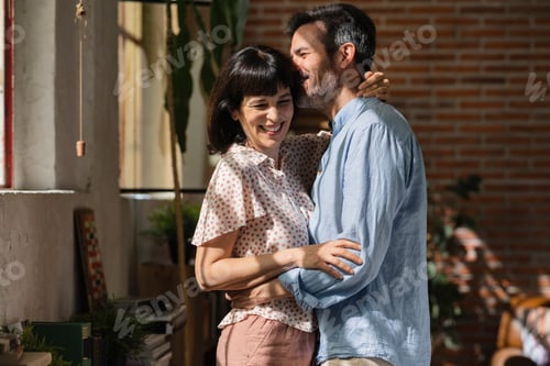 Preview: Middle aged Hispanic couple smiling happy hugging. Leaning on the window of the house.