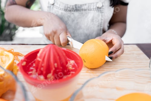 Preview: A young Hispanic woman is cutting an orange in half to make orange and carrot juice outdoors