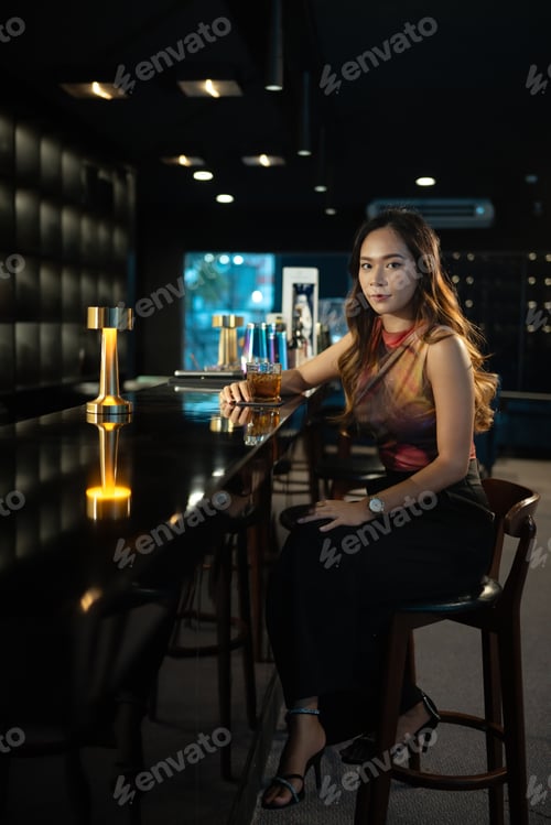 Preview: Portrait of elegant young woman relaxing with glass of whiskey at bar counter. Nightlife concept