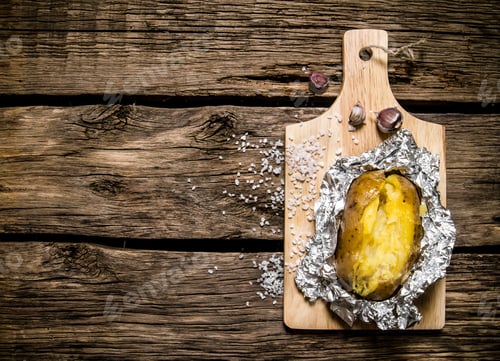 Preview: Baked potatoes in foil on a wooden table .