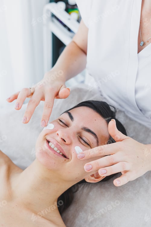 Preview: A cosmetologist applies cream to the face of a woman lying on a couch. Facial. Facial skin care