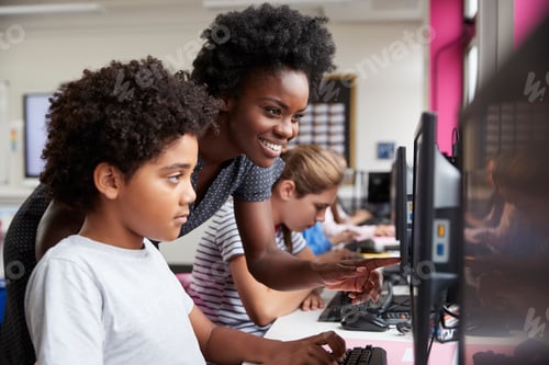 Preview: Teacher Helping Male Pupil Line Of High School Students Working at Screens In Computer Class
