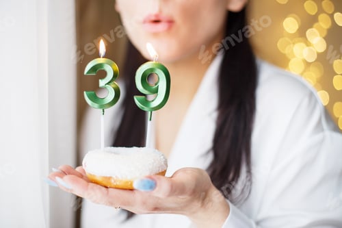 Preview: woman holding a cake with the number 39 candles on festive blurred bokeh background