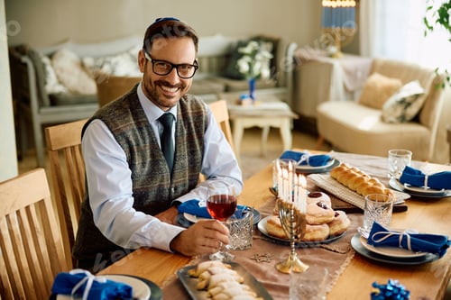 Preview: Happy Jewish man with glass of kosher wine at home looking at camera.