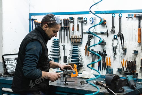 Preview: Professional mechanic using spanner while assembling vehicle engine details at workbench