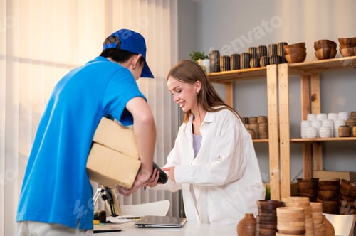 Preview: Young woman getting her cardboard box and paying via credit card to delivery man in her shop