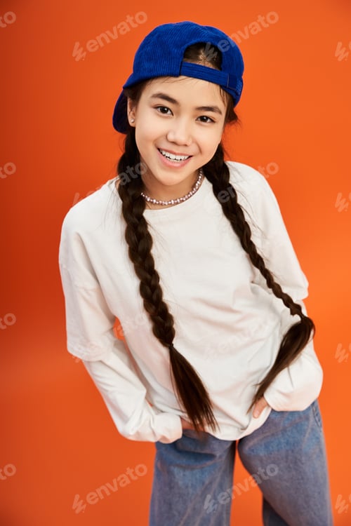Preview: Stylish teenage girl poses confidently in a vibrant studio with an orange background