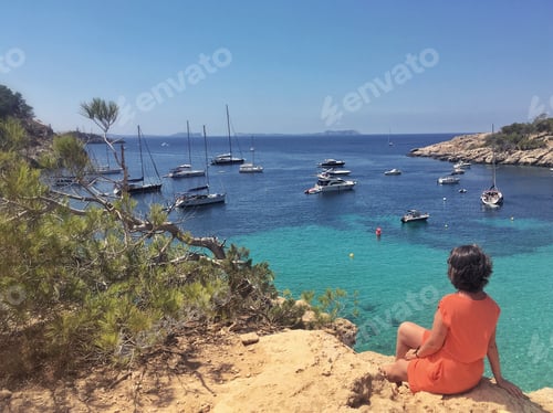 Preview: Girl is sitting on the rock with seaview. Tha bay with boats