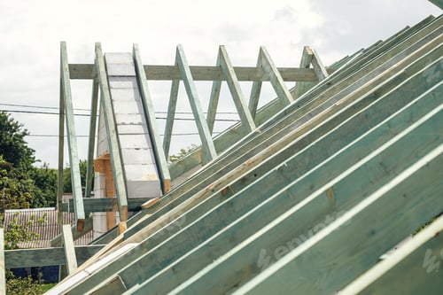 Preview: Unfinished roof trusses, view in attic with rafters and beams against sky. Wooden roof framing