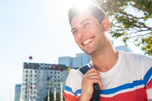 Preview: Close up laughing young man with bag in the city sun flare background