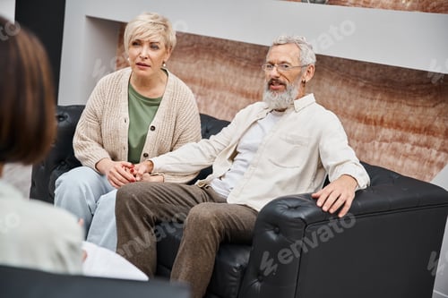 Preview: middle aged couple sitting on leather couch and looking at psychologist during family consult