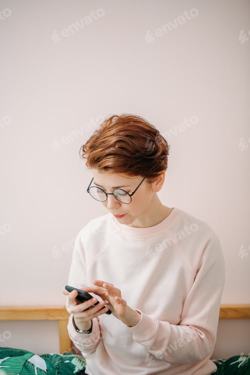 Preview: woman wearing pink sweater sitting in on pink background with smartphone