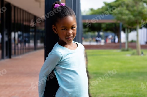 Preview: Portrait of happy biracial schoolgirl, leaning on post in schoolyard
