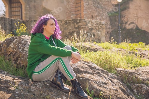 Preview: Woman with purple hair sitting on rock contemplating nature