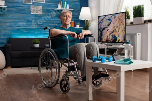 Preview: Disability senior woman in wheelchair looking at gymnastic online video on tablet computer