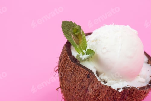 Preview: Vanilla ice cream balls in fresh coconut halves, decorated with mint leaves on a pink background