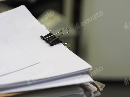 Preview: Stack of documents in focus with blurred office background, paperwork concept.