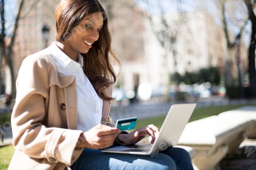 Preview: African woman shopping online sitting on a bench in a park
