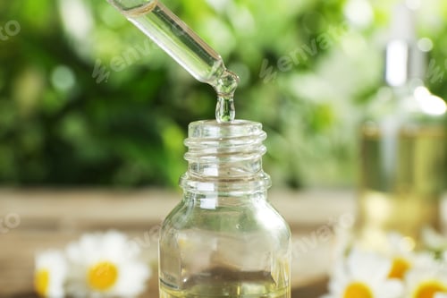 Preview: Dropping essential oil into bottle on blurred background, closeup