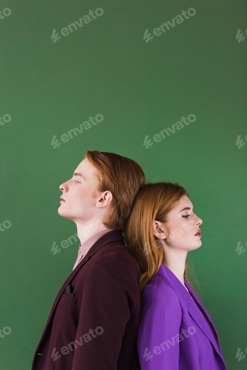 Preview: Side view of stylish couple of models standing back to back isolated on green