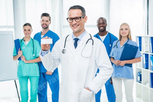 Preview: handsome mature doctor holding box of pills with colleagues standing together on background