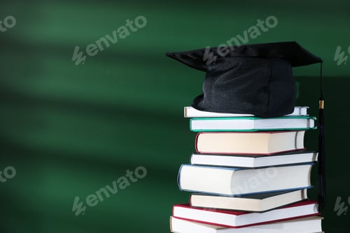 Preview: Happy Teacher's Day. Stack of books and mortarboard near chalkboard, closeup. Space for text