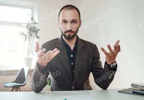 Preview: Elegance man gestuting sitting at table in daytime in office