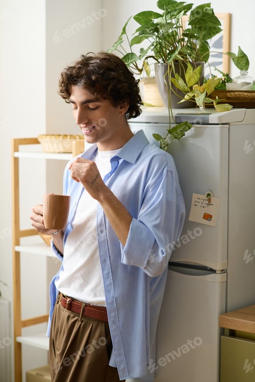 Preview: Young man enjoying a peaceful moment at home with a warm drink and a smile