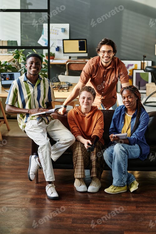 Preview: Team of young cheerful managers sitting on couch in office