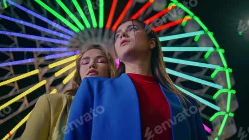Preview: Closeup girls rest ferris wheel at night. Two fashion models pose at illuminated