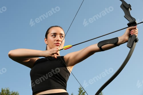 Preview: Woman with bow and arrow practicing archery outdoors, low angle view