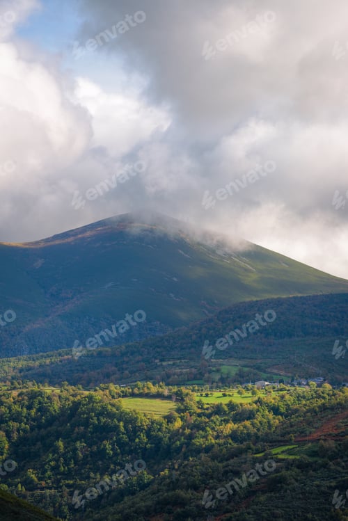 Preview: The mountainous mass of Cuinha rises between clouds over meadows and villages