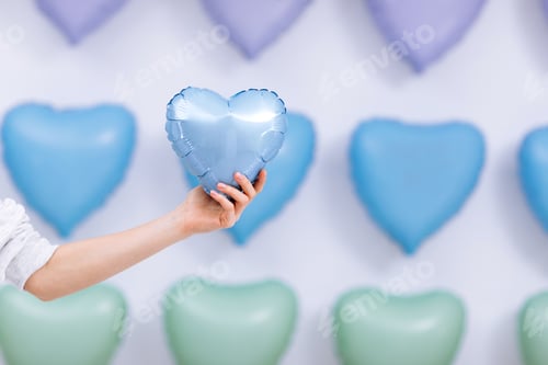 Preview: The woman holds the blue balloon in the form of a heart on many hearts background.