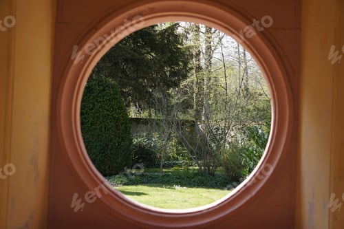 Preview: Oval window view of the outside of a house, with a lush green tree in the foreground