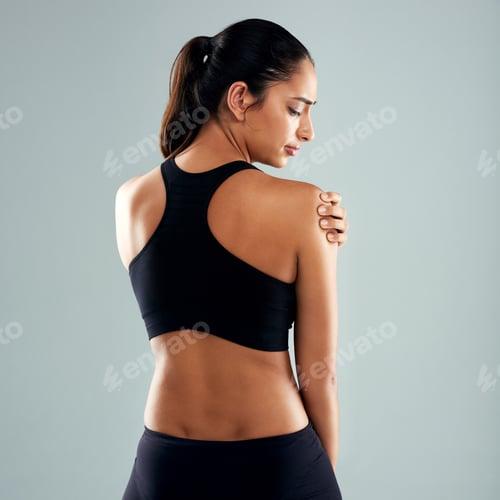 Preview: Rearview shot of a sporty young woman holding her shoulder in pain against a grey background