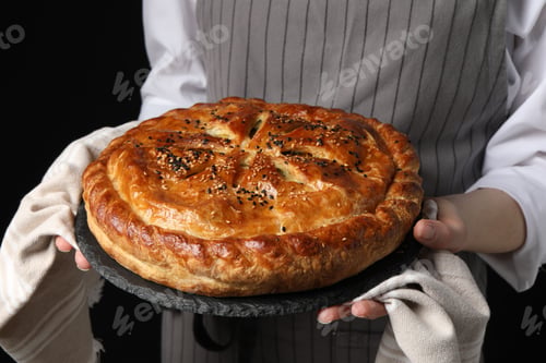 Preview: Woman holding tasty homemade pie on black background, closeup