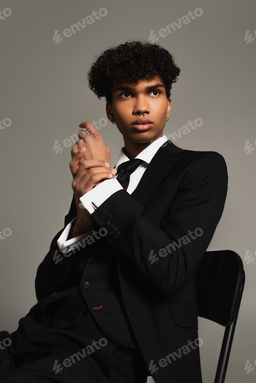 Preview: african american man in elegant three-piece suit looking away while sitting isolated on grey
