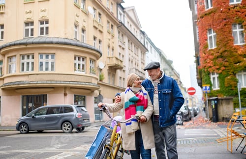 Preview: Happy senior couple with bicycle outdoors on street in city.