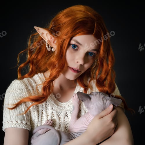 Preview: Close-up view of ginger young woman cosplayer elf in white knitted dress, cradling Sphinx kitten