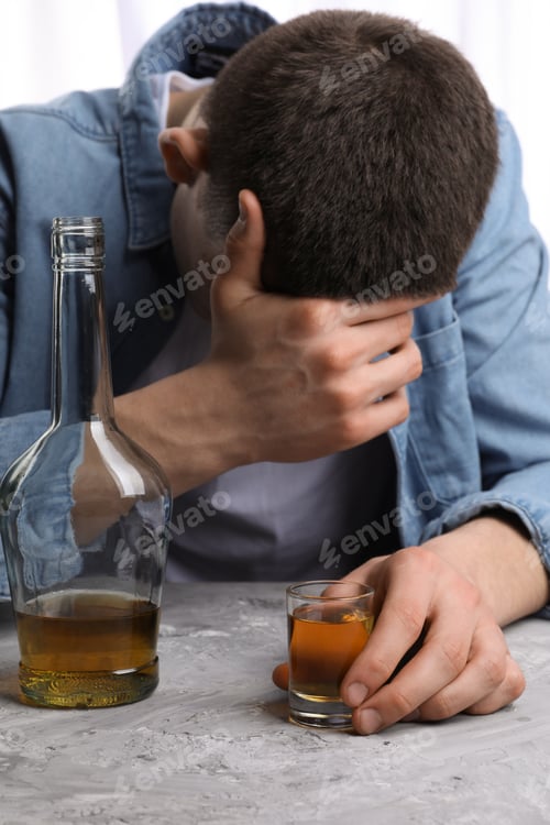 Preview: Alcohol addiction. Man with whiskey at grey textured table