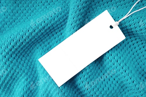 Preview: White rectangular clothing tag on turquoise knitted fabric background. Shopping, sale, discount