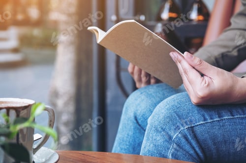Preview: a woman opening a book to read with notebooks and coffee cup on wooden table in cafe