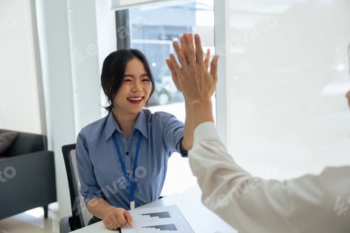 Preview: happy Asian female office worker gives high fives to a male colleague, celebrating project success