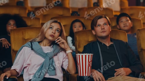 Preview: Attractive cheerful young caucasian couple laughing while watching film in movie theater.