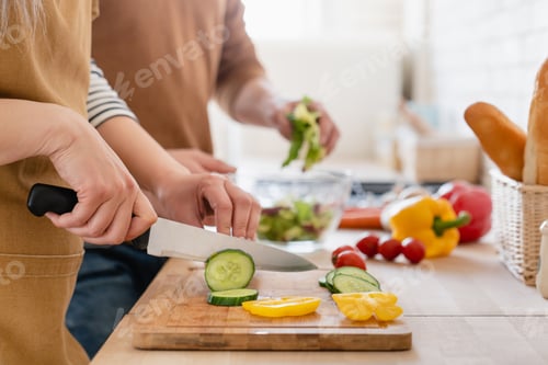 Preview: Close up cropped image of cutting board and couple cutting vegetables in the kitchen together