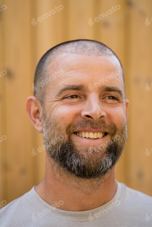 Preview: Portrait of the handsome man with beard smiling standing against wooden background