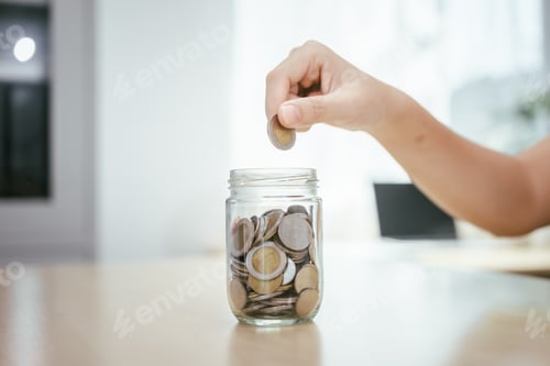Preview: A young woman saves money for the future by putting coins in a piggy bank on the table, managing